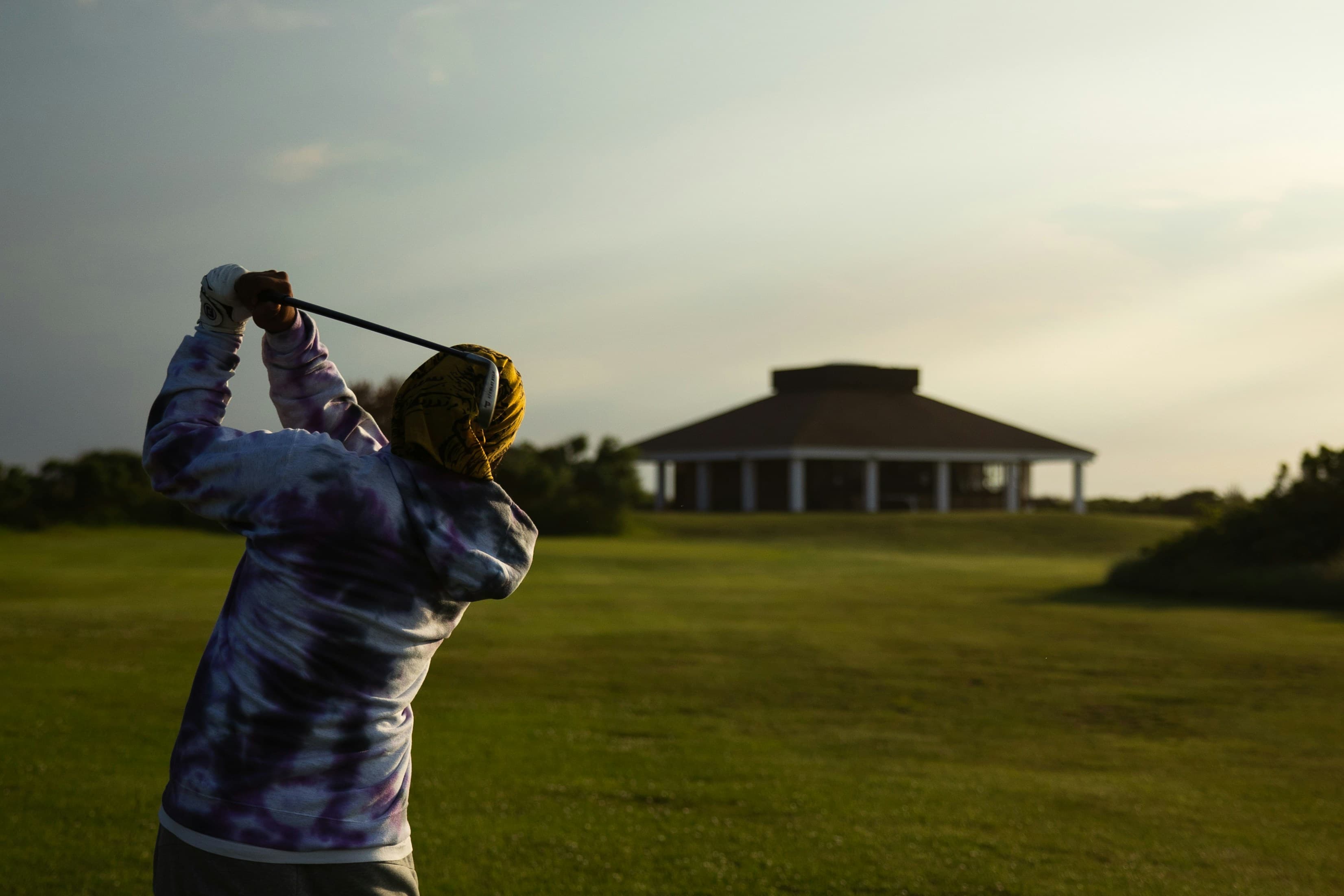 Golfeur en position de finish de swing, vu de dos, sur un fairway au coucher du soleil