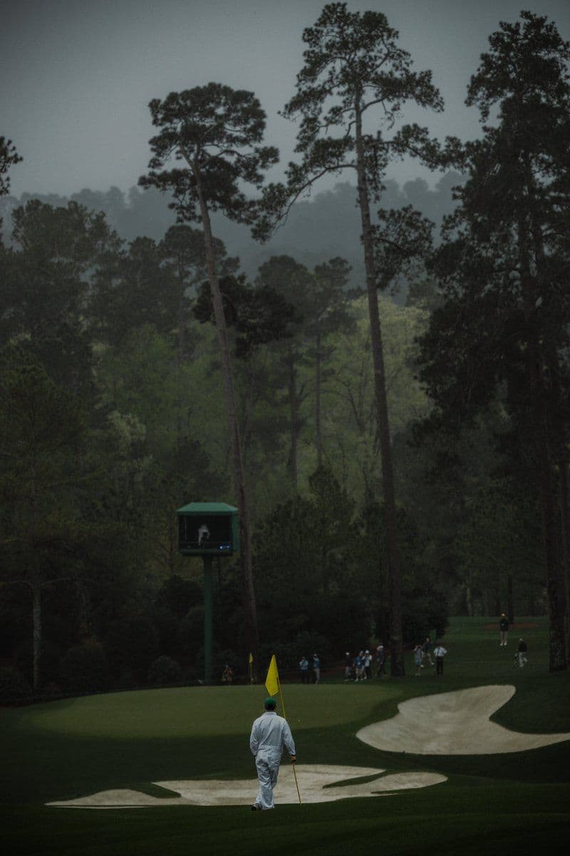 Caddie sur green de tournoi de golf sous atmosphère brumeuse, drapeau jaune en main, pression de compétition au putting